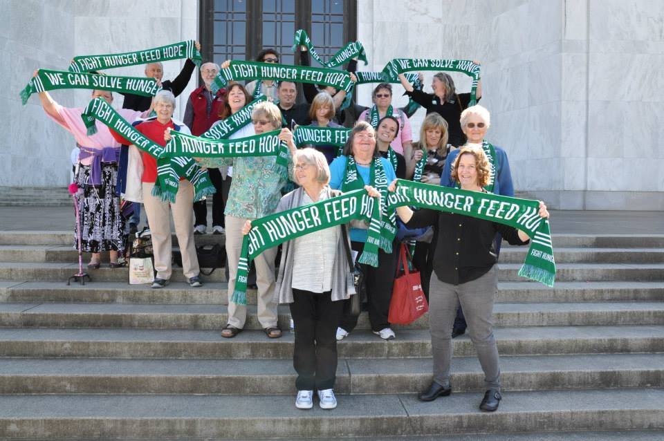 a group of people stand on the oregon state capital steps holding green scarves that say fight hunger freed hope.