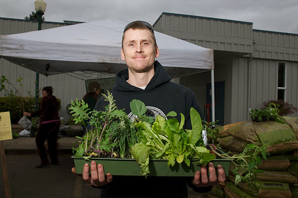 a man smiles on a grey day, holding a tray of plant starts