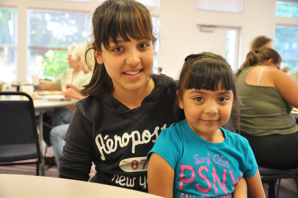 an older girl holds a younger girl in her lap. they smile into the camera.