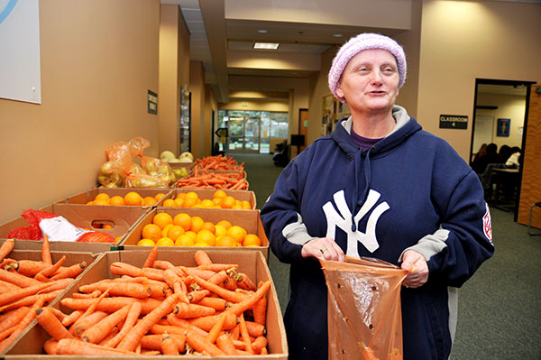 A woman with a pink hat fills a bag with vegetables next to a box of carrots