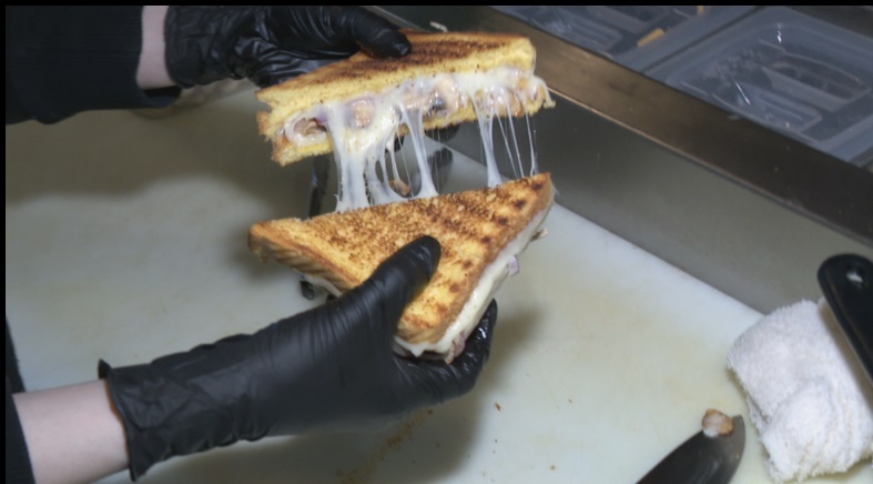 gloved hands separate two halves of a grilled cheese sandwich, cut diagonally