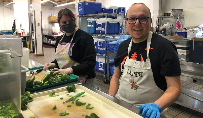 two day kitchen volunteers in aprons and gloves in front of a cutting board in the FFLC Day Kitchen