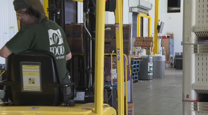 person in FOOD For Lane County t-shirt, back to camera, drives a forklift inside FFLC's Bailey Hill Rd. warehouse