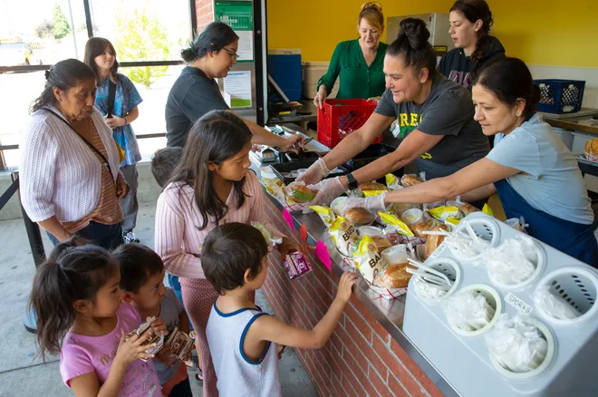 workers serve meals to kids lined up with caregivers