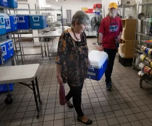 Laura Cole, left, and Lee Temple volunteer once a week to deliver for FOOD For Lane County's Meals on Wheels program. They carry a blue cooler between them through FFLC's kitchen.