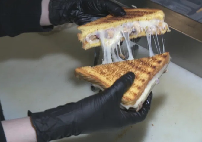 two hands in black latex gloves tear apart a grilled cheese sandwich cut diagonally